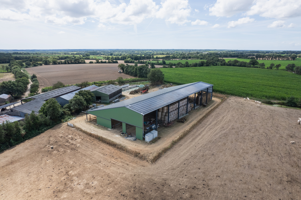 Vue aérienne d'une exploitation agricole comprenant un hangar agricole photovoltaïque avec espace de stockage, entourée de champs verdoyants.